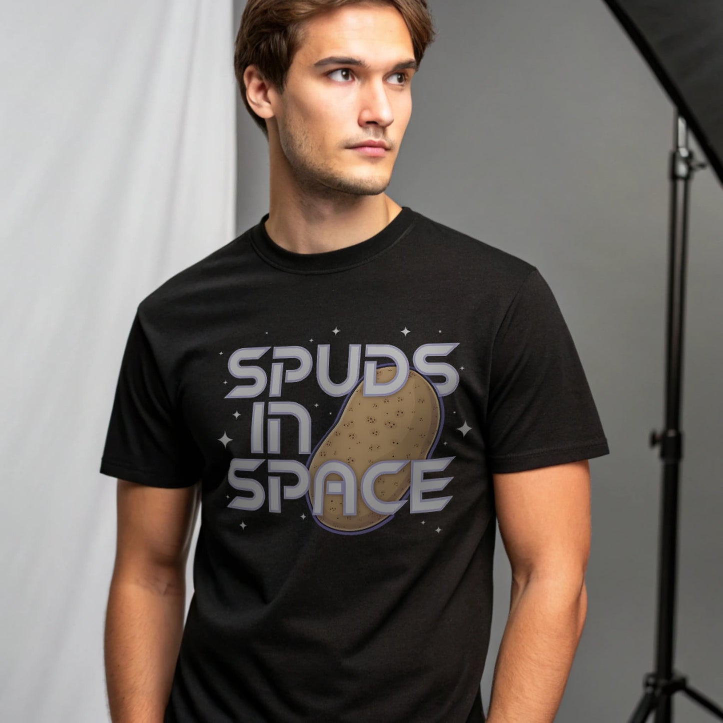 Male model wearing a black crew-neck t-shirt with “Spuds in Space” graphic, studio portrait on a grey background.