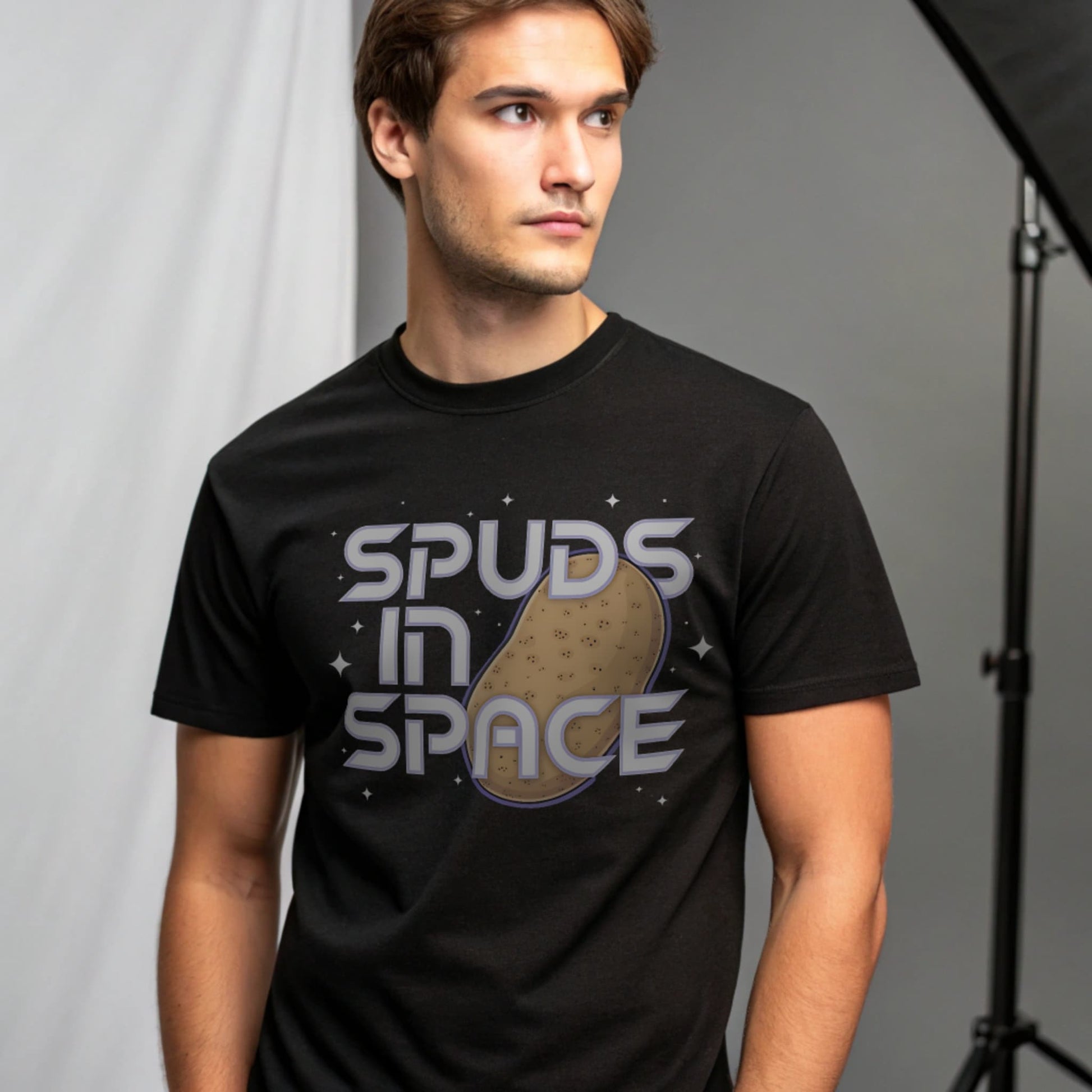 Male model wearing a black crew-neck t-shirt with “Spuds in Space” graphic, studio portrait on a grey background.