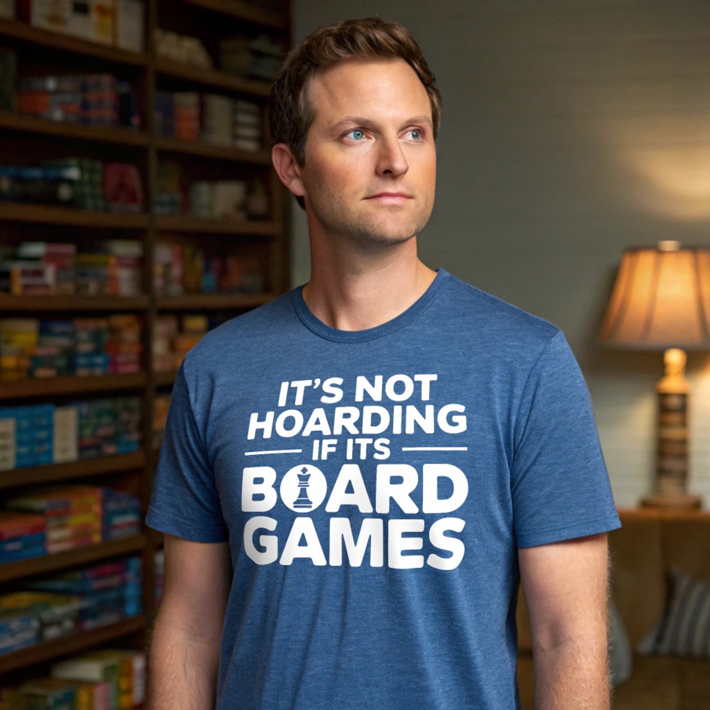 Hyper-realistic mockup of a 25–40-year-old man wearing a heather indigo Board Games Hoarder T-Shirt standing in a cozy game room with floor-to-ceiling shelves of board-game boxes.