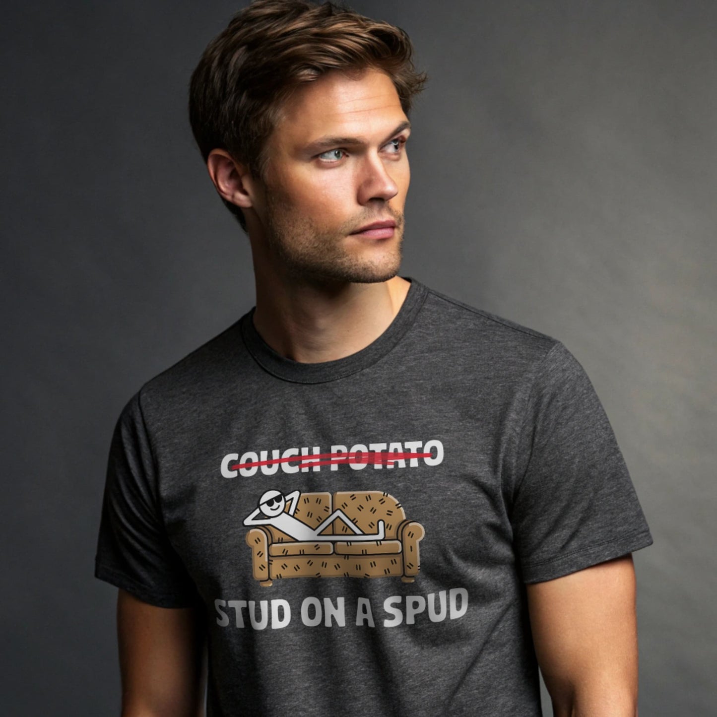 Male model wearing a dark heather crew-neck t-shirt with “Couch Potato: Stud on a Spud” graphic, studio shot on gray backdrop.