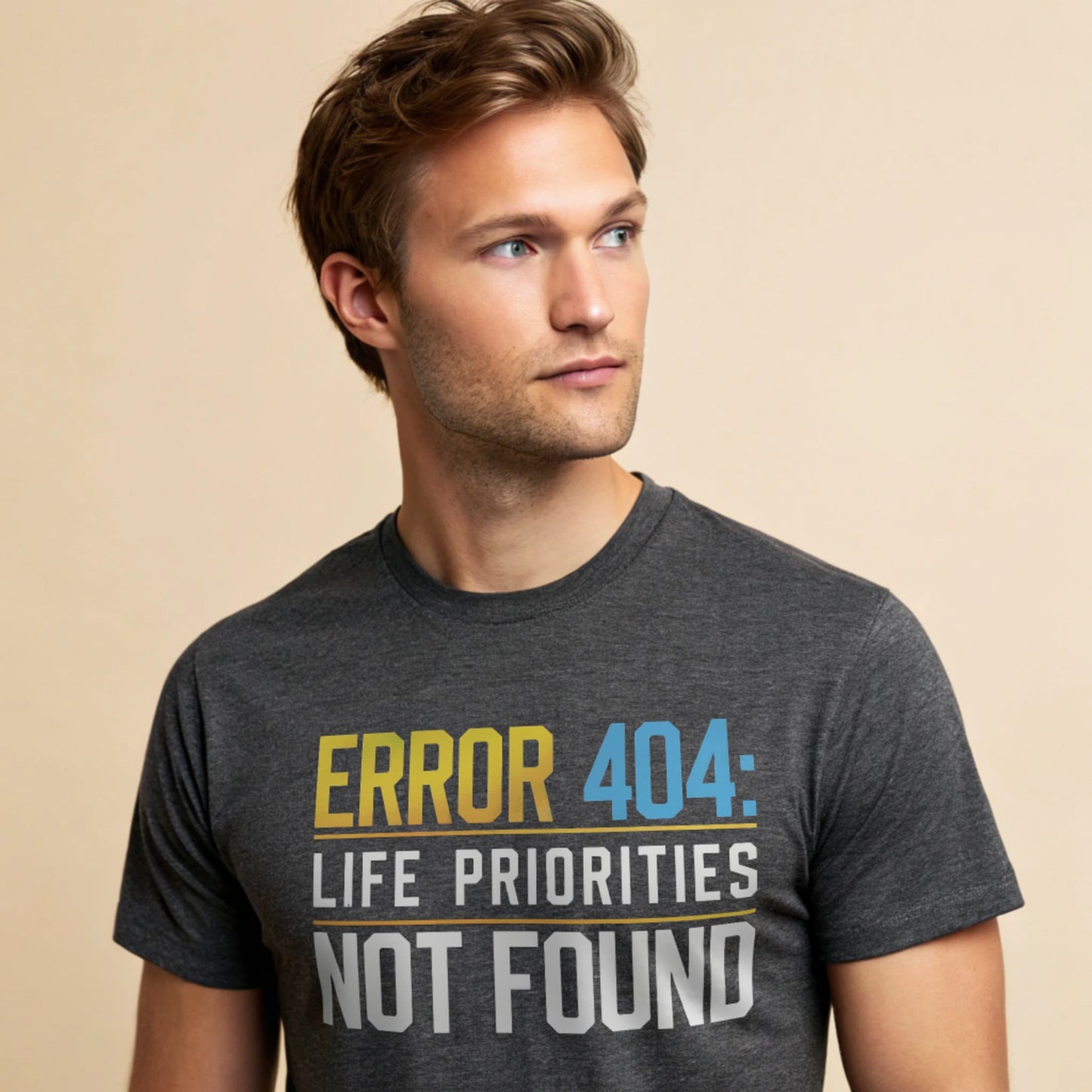 Male model wearing a dark heather crew-neck t-shirt with “Priorities Not Found” tech graphic, studio shot on a warm-beige background.
