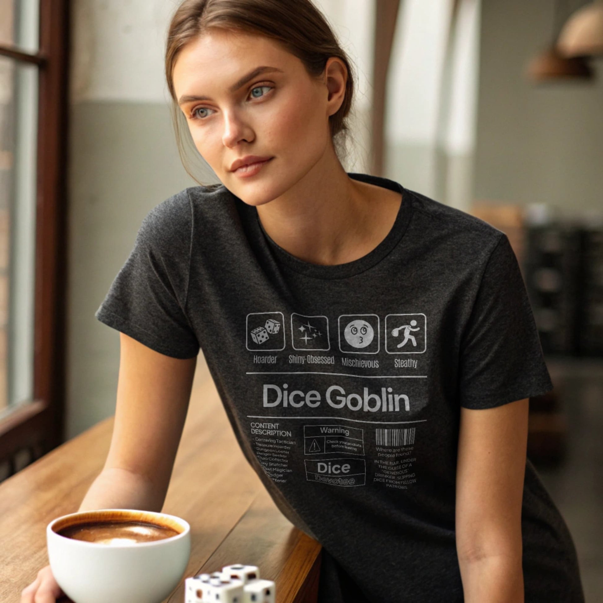 Dark Heather lifestyle mockup of Dice Goblin T-Shirt on a female model at a café table with espresso and dice bowl
