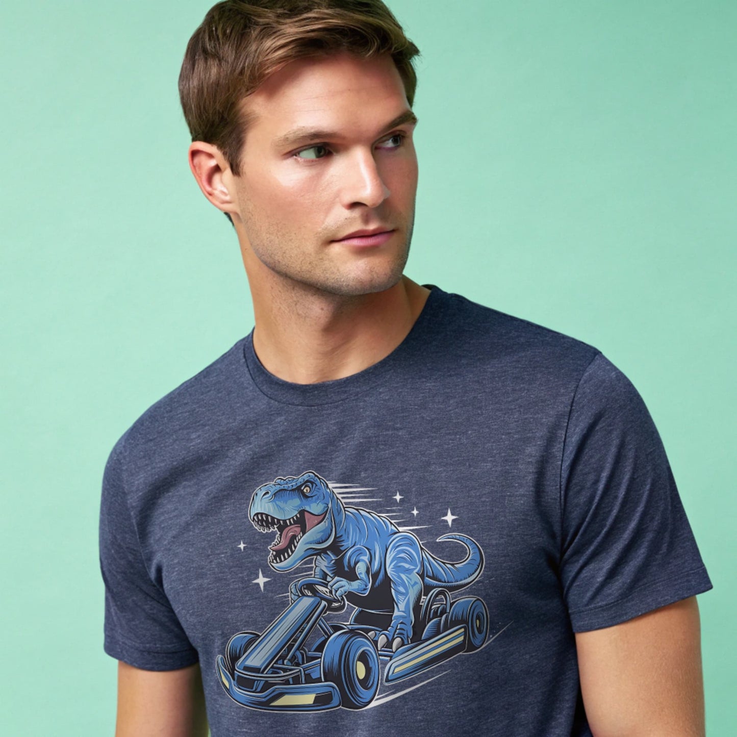 Male model wearing a heather navy crew-neck t-shirt with a blue dinosaur kart graphic, studio shot on a smooth mint-green background.