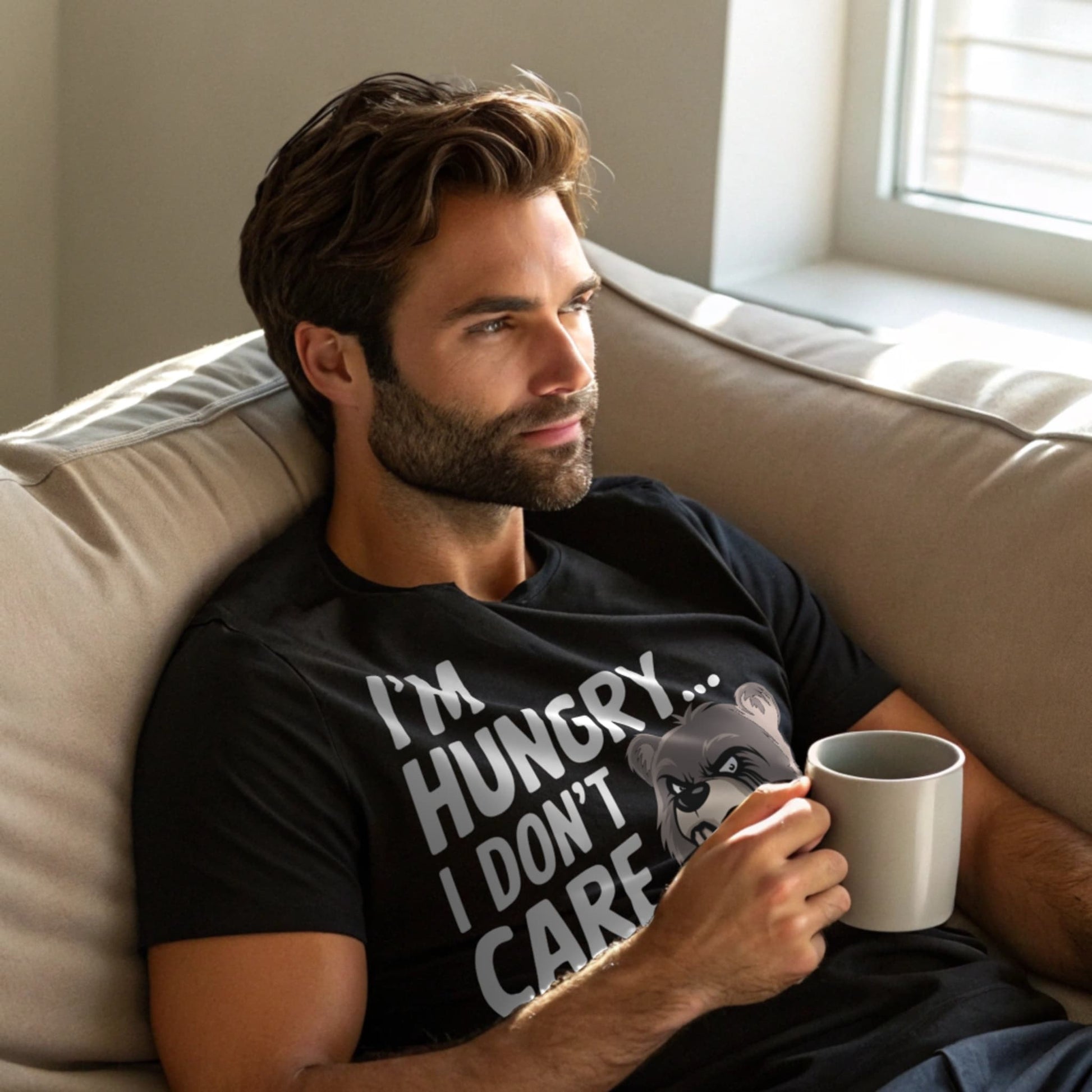 Man lounging with coffee in black “I’m Hungry… I Don’t Care” t-shirt on couch in daylight