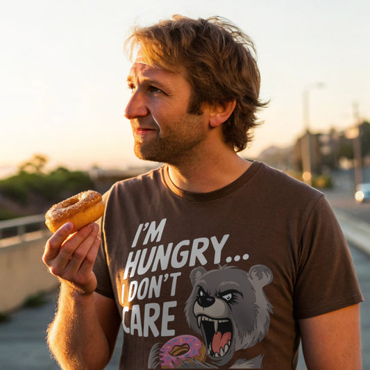 Man wearing brown “I’m Hungry… I Don’t Care” t-shirt holding a donut outside at sunset