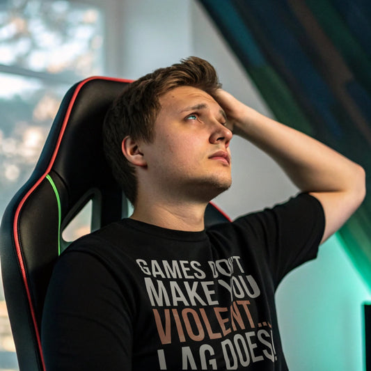 Man in black gaming shirt sitting in RGB-lit room with frustrated expression, shirt says “Games Don’t Make You Violent… Lag Does”