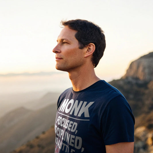 Man standing on a mountain at sunrise wearing Monk Mode: Unhinged T-Shirt, calm and centered