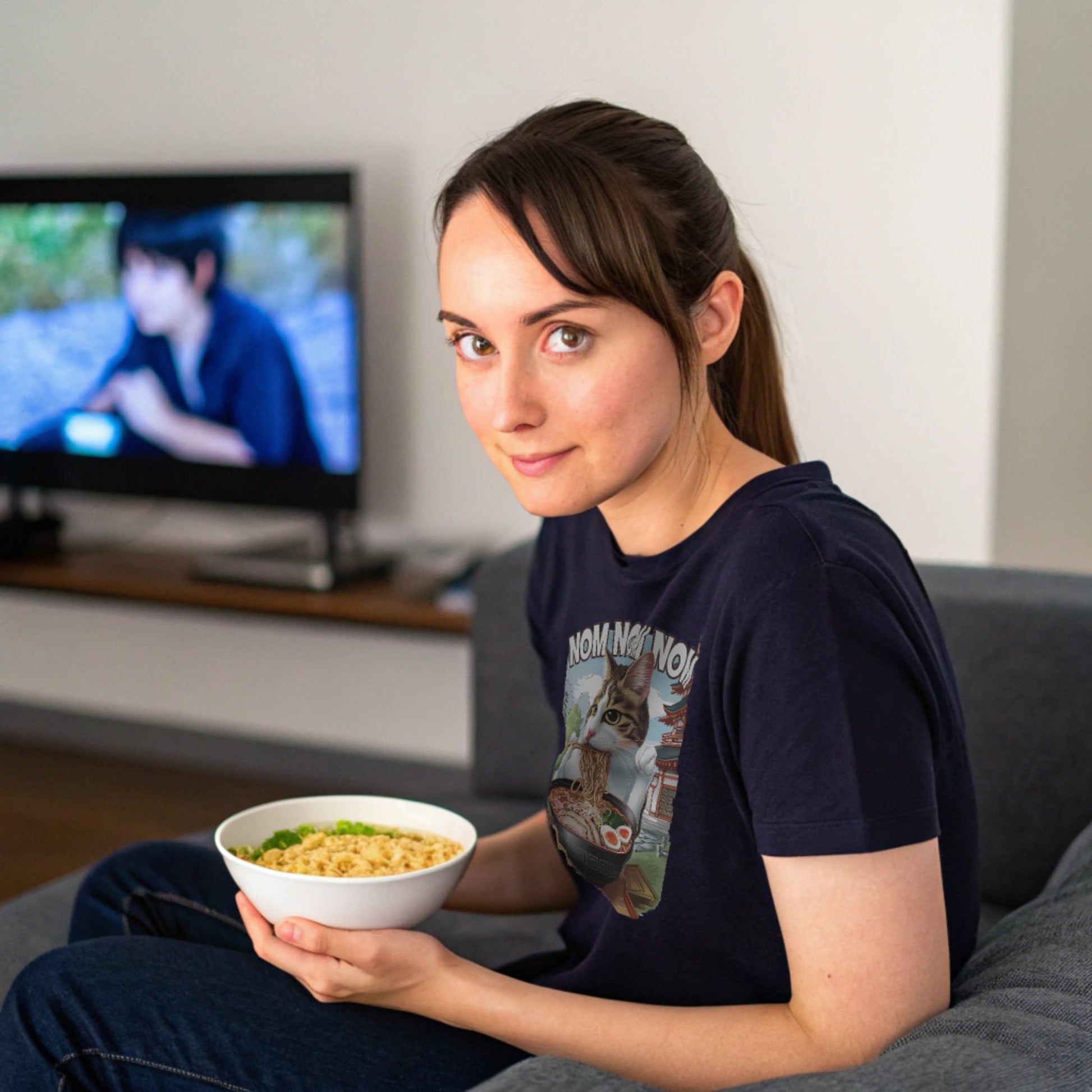 Navy lifestyle mockup of Ramen Cat T-Shirt on a female model curled up on a couch with a bowl of ramen, watching anime
