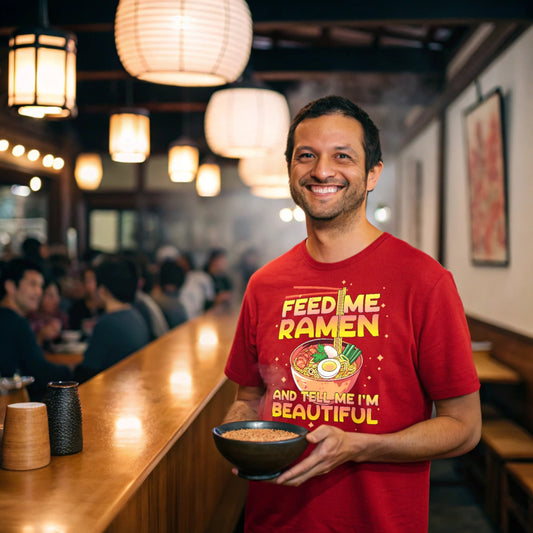 Smiling man in a ramen shop wearing a red Ramen Lover T-Shirt and holding a bowl.