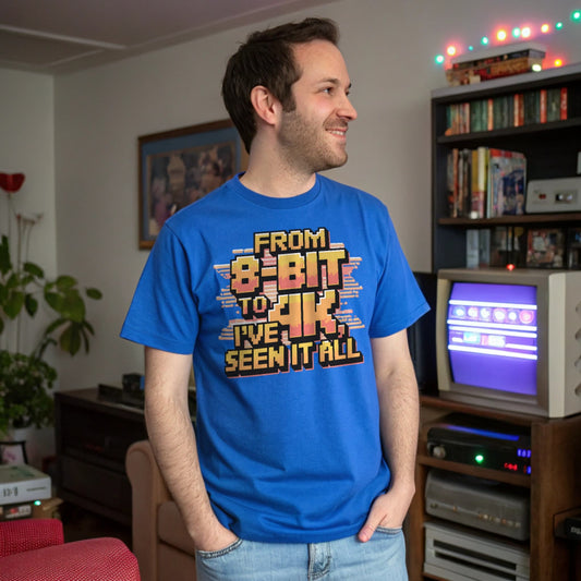 Man wearing royal blue retro gaming shirt that says “From 8-Bit to 4K, I’ve Seen It All,” standing in a nostalgic gaming-themed room.