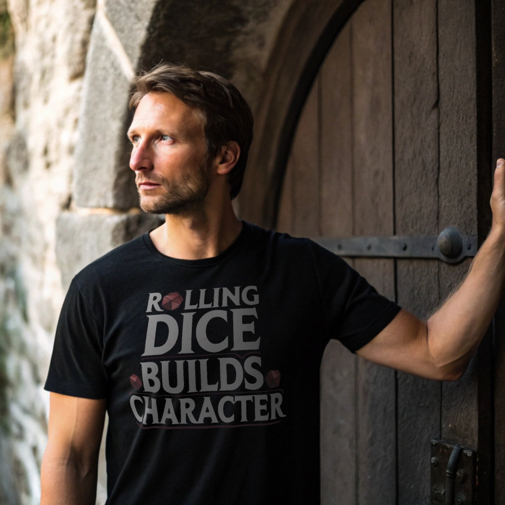 Black lifestyle mockup of Rolling Dice Builds Character tee in front of an ancient stone dungeon door, male model hand on handle