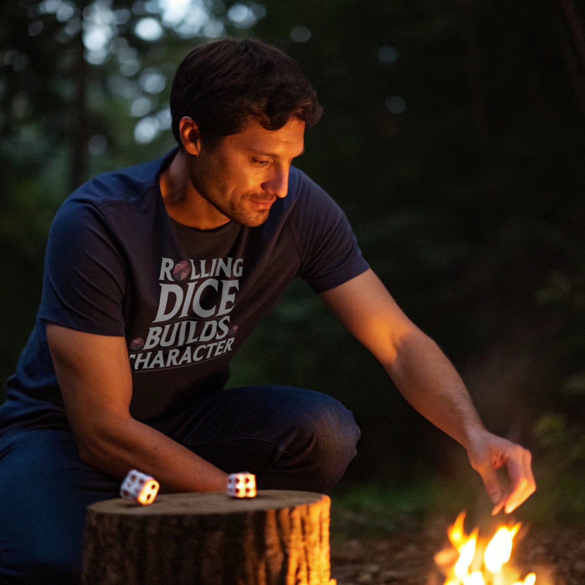 Navy lifestyle mockup of Rolling Dice Builds Character tee crouched by a glowing campfire tossing dice, male model natural eyes