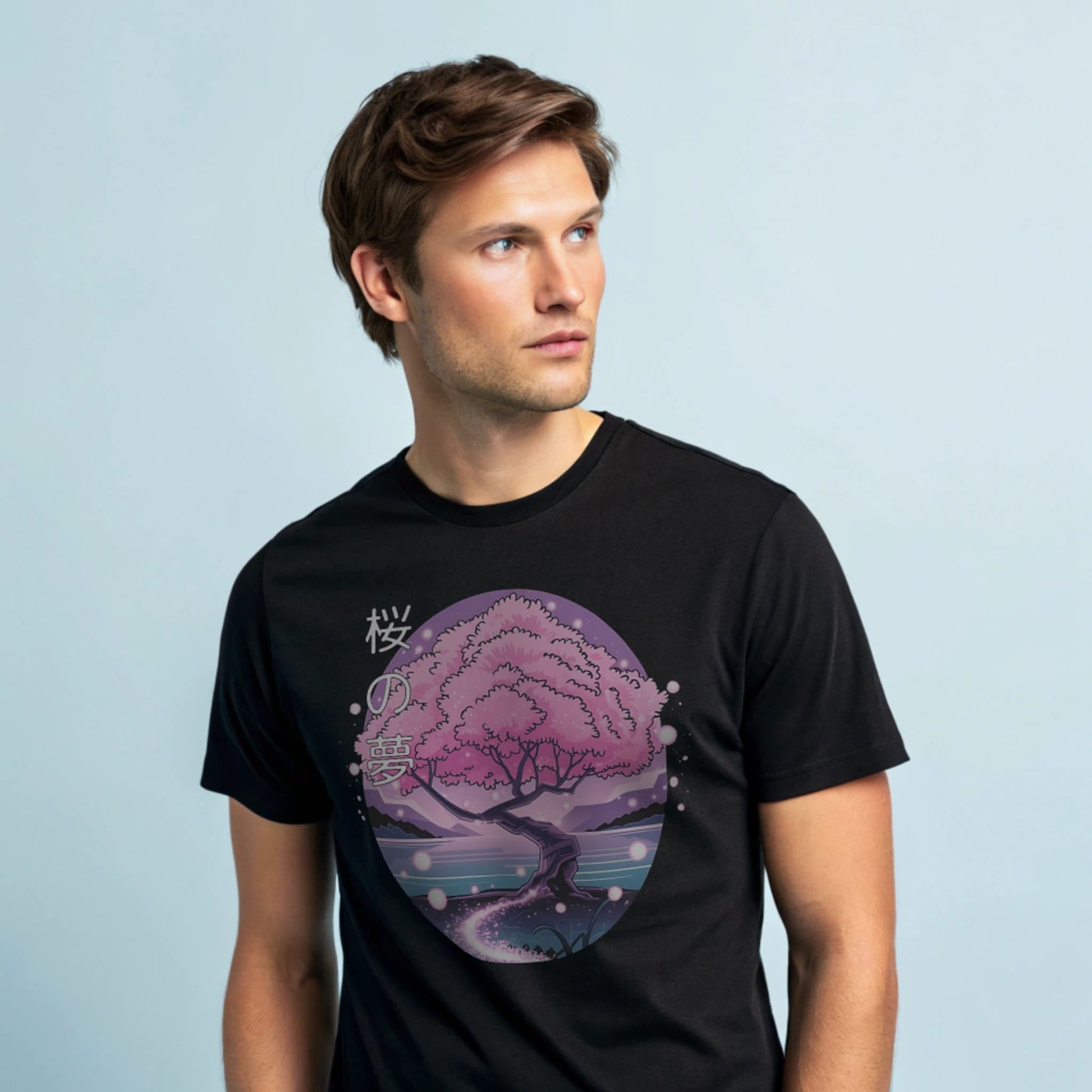 Male model wearing a black crew-neck t-shirt with pink cherry-tree graphic, studio shot on a smooth pale-blue background.