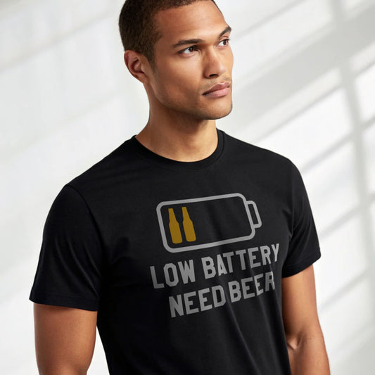 Male model wearing a black crew-neck t-shirt with a low battery icon and “Low Battery Need Beer” text, studio shot on white drape backdrop