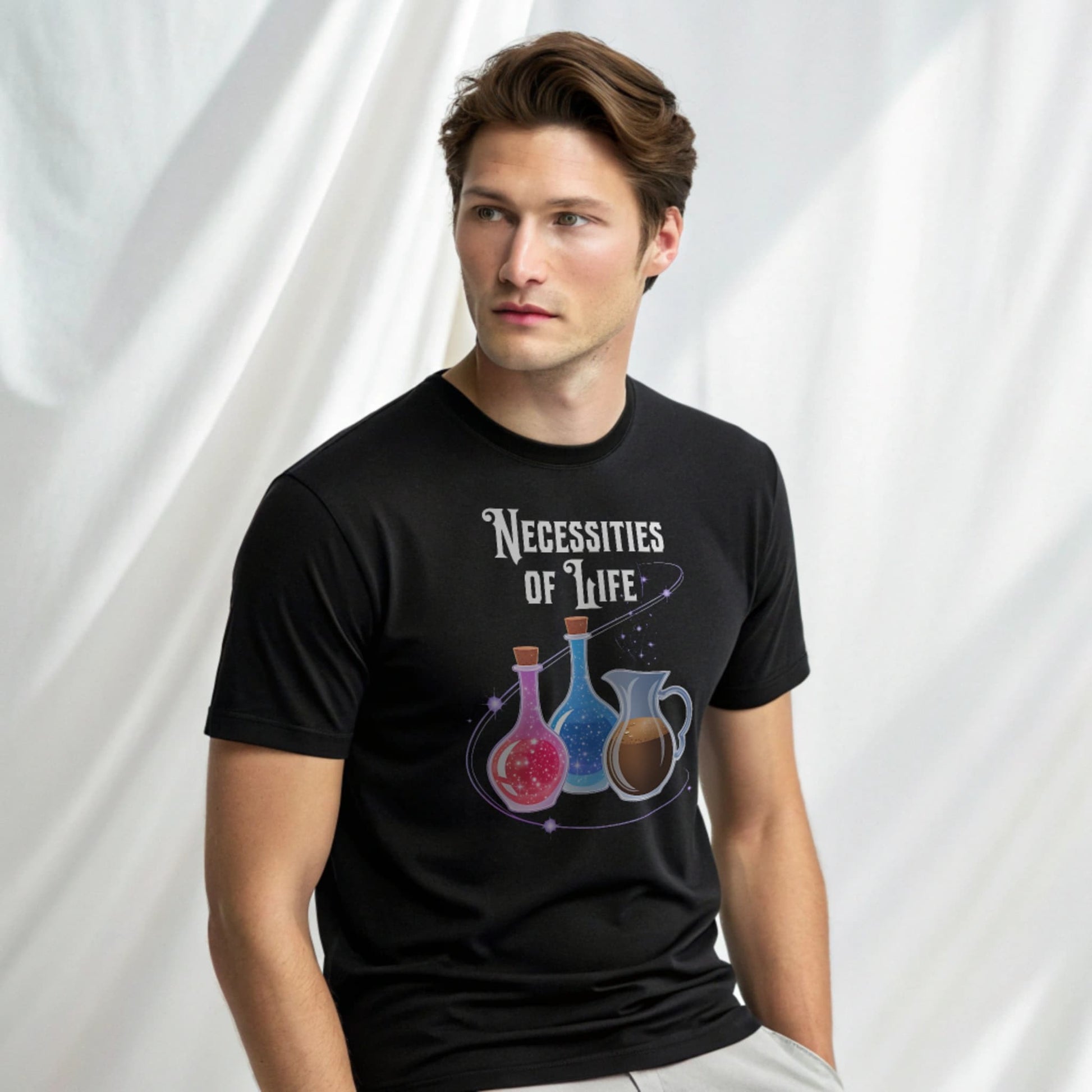 Male model in a black crew-neck t-shirt with “Necessities of Life” potion graphic, studio shot on white drape background.