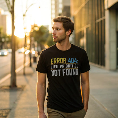 Male model walking an urban sidewalk in a black crew-neck t-shirt with “Priorities Not Found” tech graphic, lifestyle street shot at golden hour.