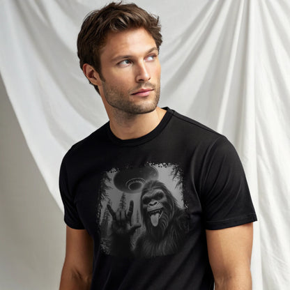 Male model wearing a black crew-neck t-shirt featuring a white silhouette of Sasquatch raising its hand graphic, studio shot on a white drape backdrop.