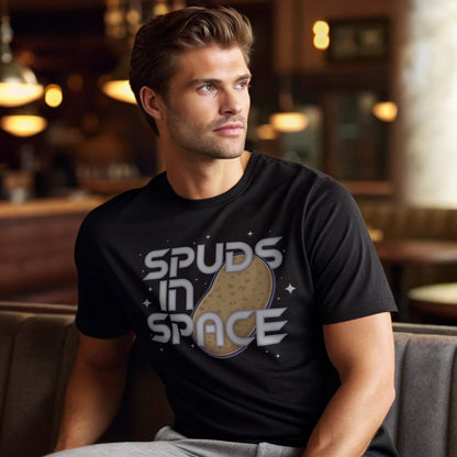 Male model lounging in a café interior in a black crew-neck t-shirt with “Spuds in Space” graphic, lifestyle indoor shot.