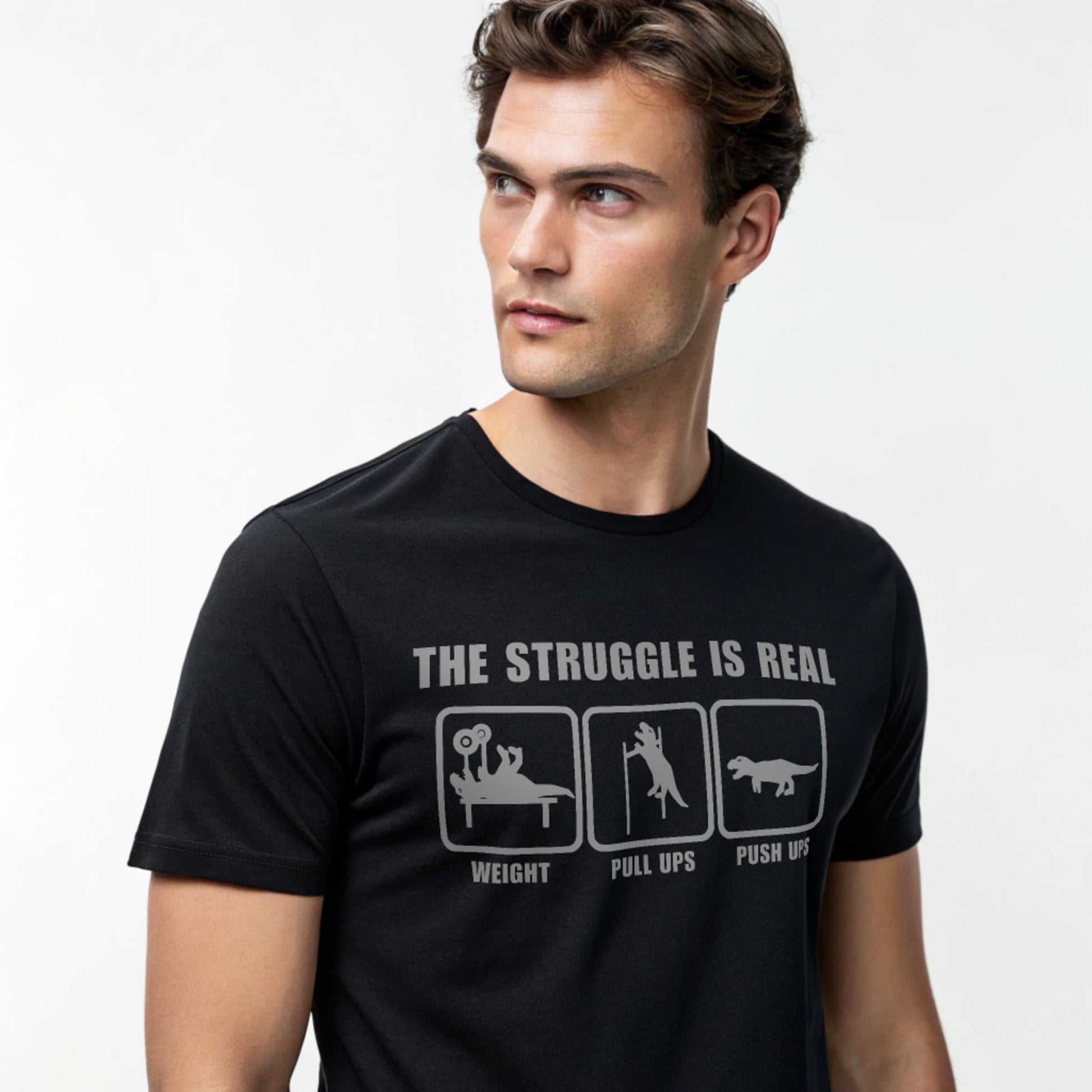 Male model wearing a black crew-neck t-shirt with “The Struggle Is Real” graphic, studio shot on a white backdrop.