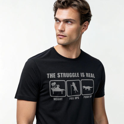 Male model wearing a black crew-neck t-shirt with “The Struggle Is Real” graphic, studio shot on a white backdrop.