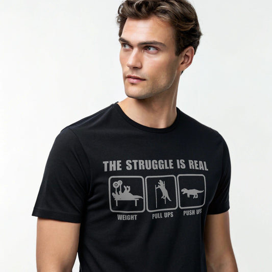 Male model wearing a black crew-neck t-shirt with “The Struggle Is Real” graphic, studio shot on a white backdrop.