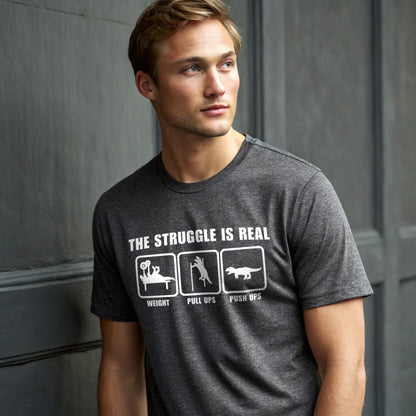 Male model wearing a dark heather crew-neck t-shirt with “The Struggle Is Real” graphic, studio shot on a dark gray backdrop.