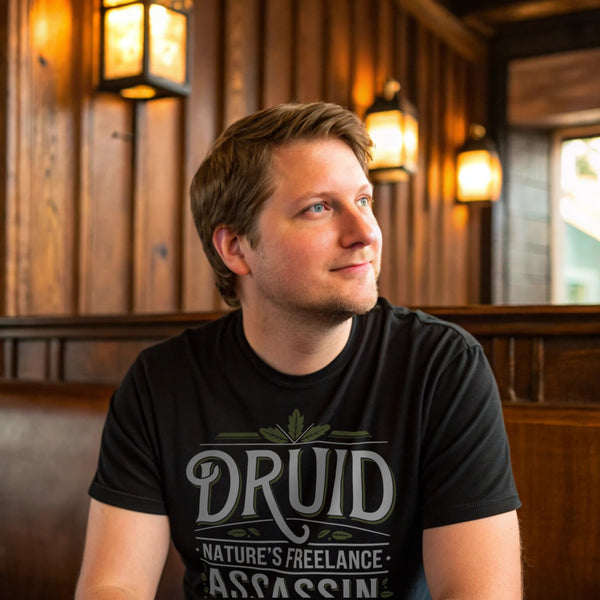 Man wearing black Druid: Nature’s Freelance Assassin T-Shirt inside a rustic bar, casual lighting, realistic crew neck tee