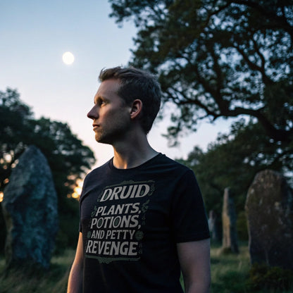Black lifestyle mockup of Druid Petty Revenge T-Shirt on a male model inside a stone circle under twilight sky, plain crew neck