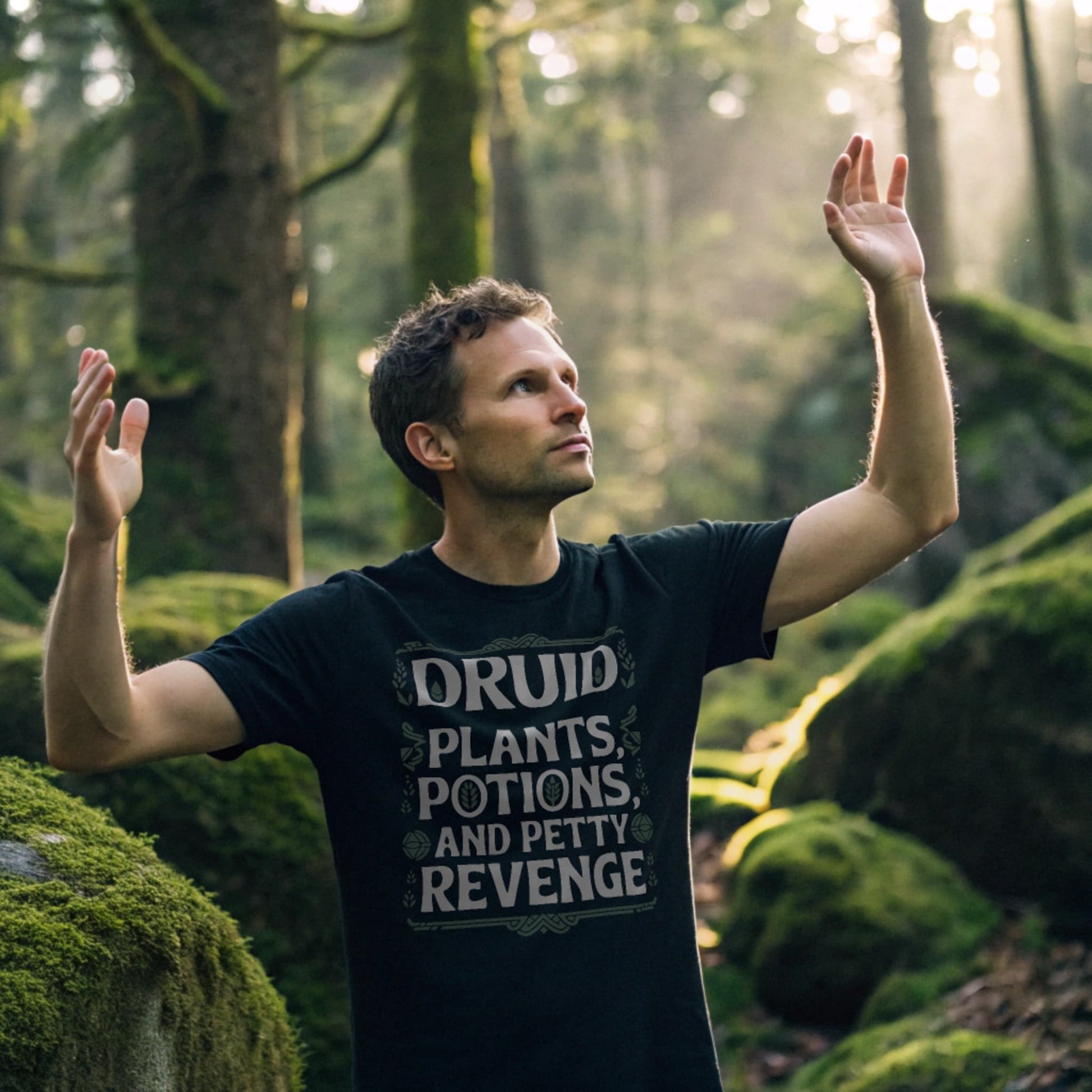 Black lifestyle mockup of Druid Petty Revenge T-Shirt on a male model standing in a sun-dappled forest clearing, plain crew neck