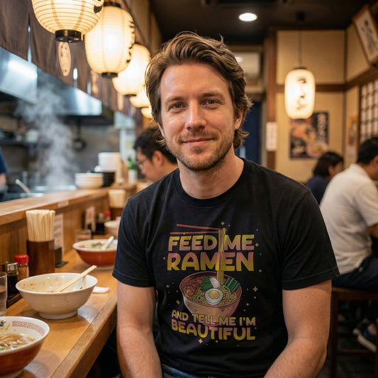 Man sitting in a cozy ramen shop wearing the “Feed Me Ramen and Tell Me I’m Beautiful” t-shirt