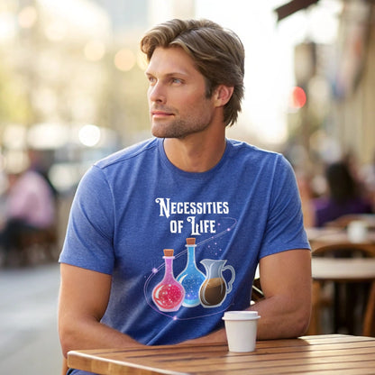 Male model in a heather royal crew-neck t-shirt with “Necessities of Life” potion graphic, window-lit studio shot.