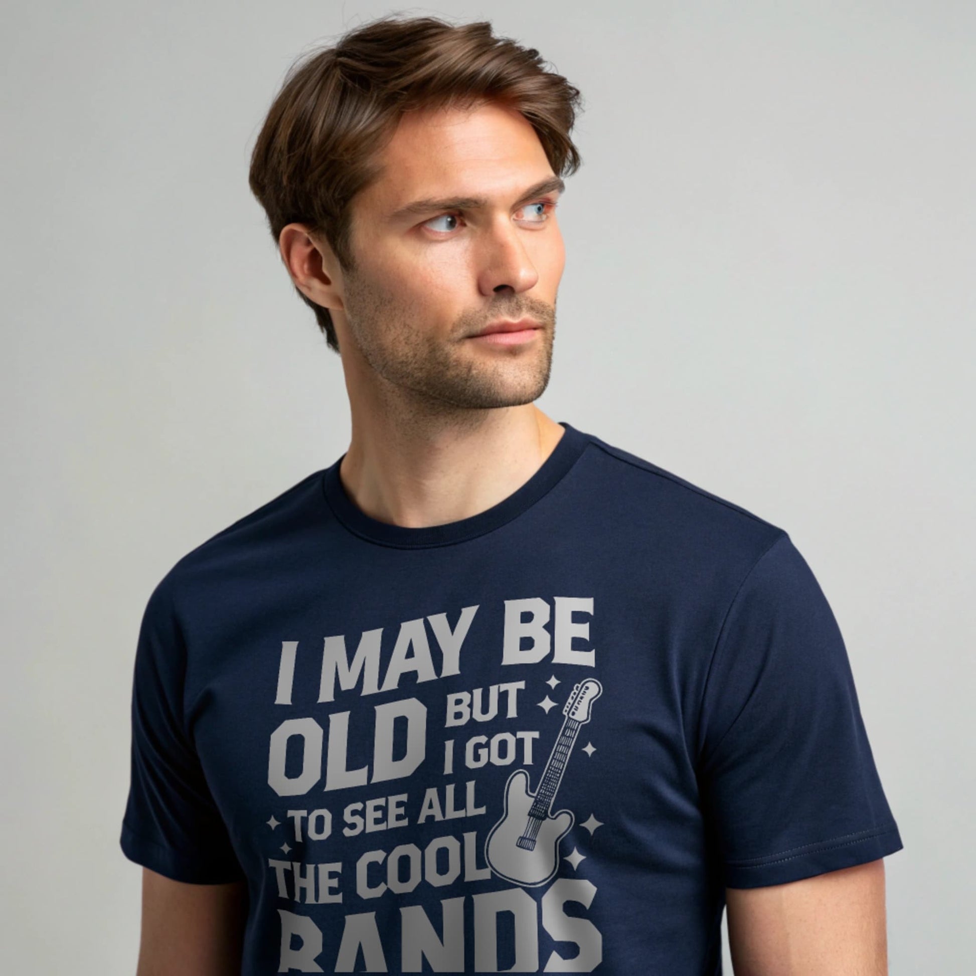 Male model wearing a navy crew-neck t-shirt with a vintage guitar graphic and “I May Be Old But I Got To See All The Cool Bands” text, studio shot on a smooth pale-gray background.