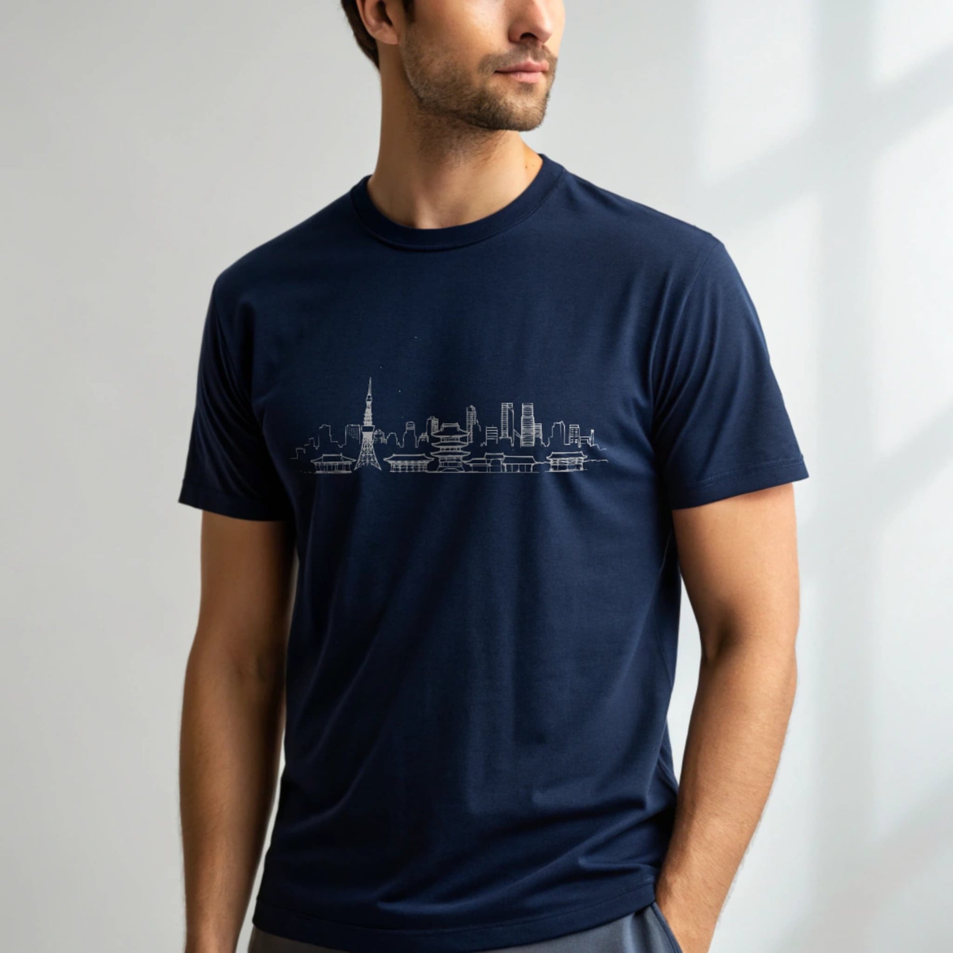 Male model wearing a navy crew-neck t-shirt with a white city skyline graphic, studio shot on a smooth light-gray background.