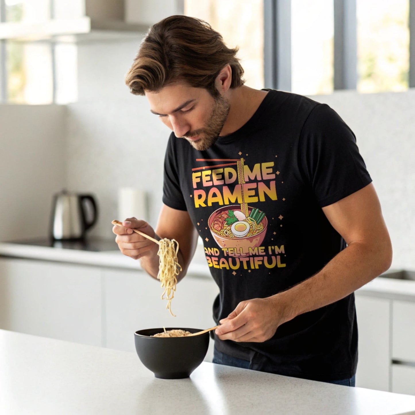 Man slurping ramen in a modern kitchen while wearing a black Ramen Lover T-Shirt.