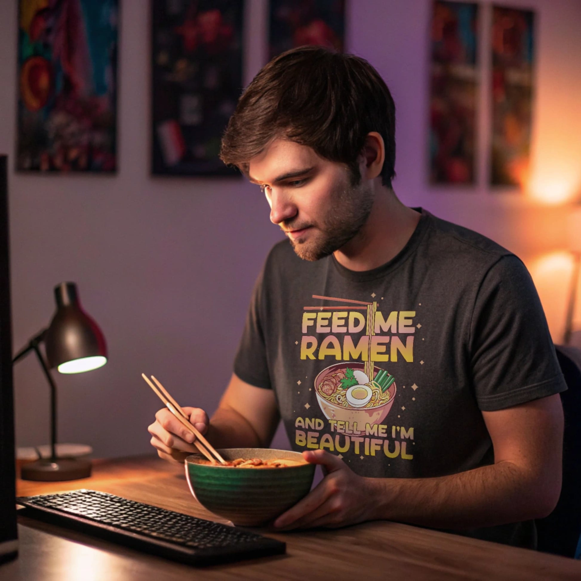 Late-night gamer at a desk, slurping ramen while wearing a charcoal Ramen Lover T-Shirt.