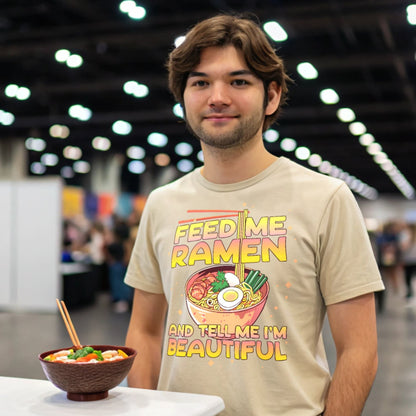 Otaku at a convention wearing a natural-colored Ramen Lover T-Shirt beside a ramen bowl.