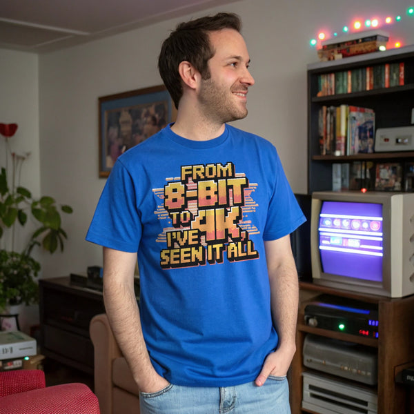 Man wearing royal blue retro gaming shirt that says “From 8-Bit to 4K, I’ve Seen It All,” standing in a nostalgic gaming-themed room.