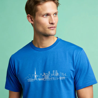 Male model wearing a royal blue crew-neck t-shirt with a white city skyline graphic, studio shot on a smooth mint-green background.