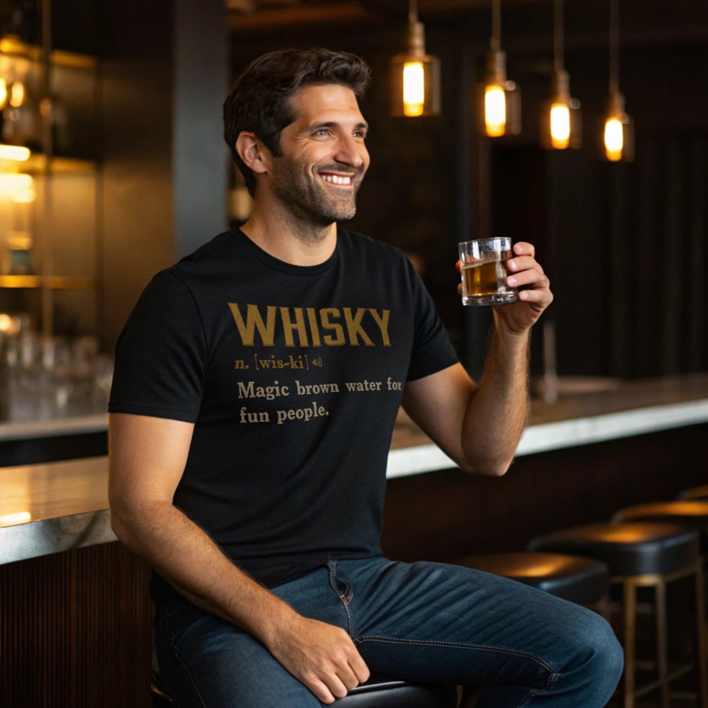 Lifestyle mockup of smiling man at a bar wearing the Black Whisky Definition T-Shirt and holding a whisky glass.