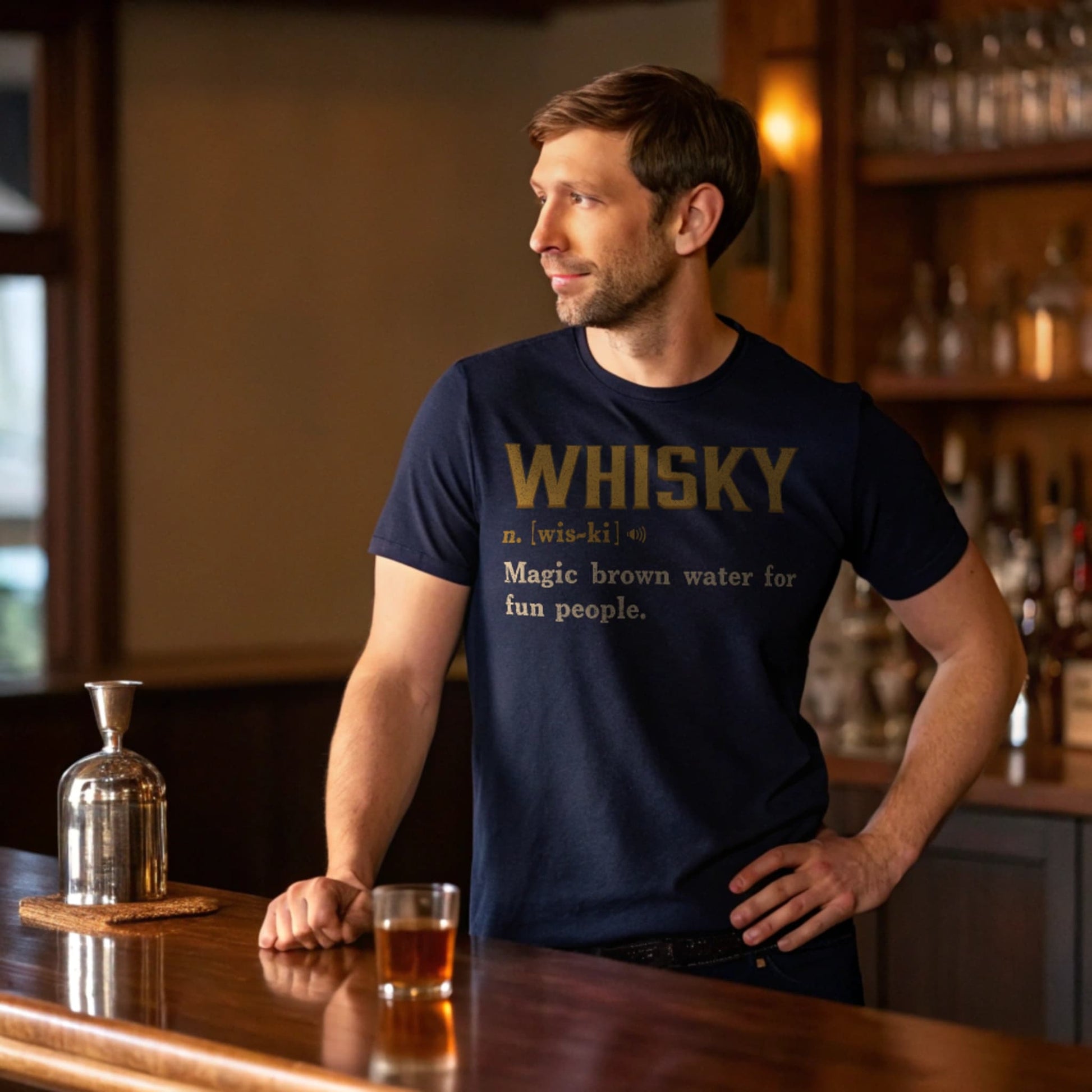Lifestyle mockup of a man at a home bar wearing the Navy Whisky Definition T-Shirt, glass and decanter visible.